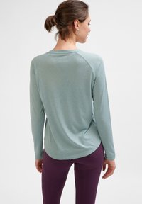 Himmelblaues Langarmshirt mit abgerundetem Saum, Raglanärmeln und strukturierter Stoffqualität, kombiniert mit lila Leggings.