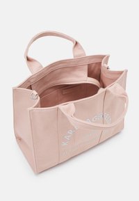 Sac fourre-tout en toile rose avec deux poignées supérieures, une poche intérieure zippée et un texte logo blanc sur le devant. Léger avec des côtés structurés.