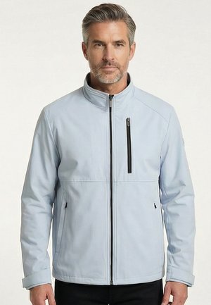 Man die naar voren kijkt, draagt een lichtblauwe jas met rits en een hoge kraag, met een borstzak met rits, staand tegen een effen achtergrond.