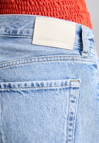 Light blue denim jeans feature a distinct top-stitching design, a leather patch labeled "CITIZENS of HUMANITY," and a classic five-pocket style.