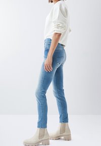 Jeans ajustados de mezclilla azul claro con una cintura alta, combinados con botas de tobillo beige que tienen una suela gruesa y elásticos laterales.