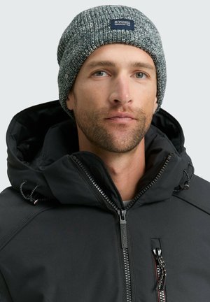 Zwarte jack met capuchon, voorzien van een ritssluiting aan de voorkant en ritszakken. Grijze gebreide beanie met een gestructureerde afwerking en een logo patch.