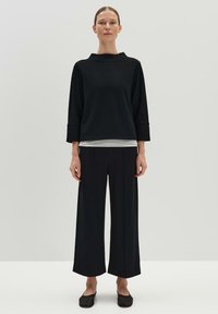 Haut noir à manches longues avec un col montant, associé à un pantalon noir à jambes larges. Texture lisse, design minimal, lignes épurées et palette de couleurs monochrome.