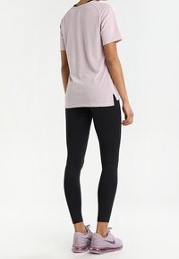 Rosa Sport-T-Shirt mit strukturiertem Muster, kurzen Ärmeln und schwarzen Akzenten. Schwarze Leggings und helllila Sneakers mit sichtbarer Dämpfung.