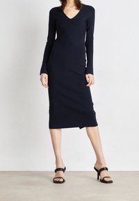 Robe tricotée à manches longues, de couleur bleu marine foncé, avec un col en V et une silhouette ajustée, présentant un motif géométrique subtil et une longueur mi-mollet.