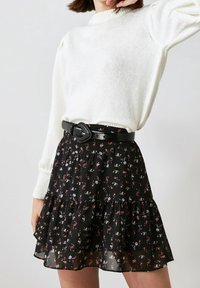 Zwarte bloemenrok met gelaagde ruches, voorzien van een rood-wit bloemenpatroon. Gepaard met een witte sweatshirt met textuur en een zwarte riem.