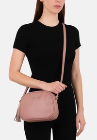 Borsa a tracolla in pelle rosa con un design elegante, hardware dorato e un dettaglio a frangia. Cinghia regolabile e chiusura a zip. Texture liscia.