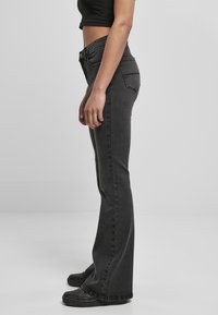 Svarta utsvängda jeans med midjhöjd, tillverkade av denim. Har två bakfickor och en lätt stretch. Matchas med svarta skor.