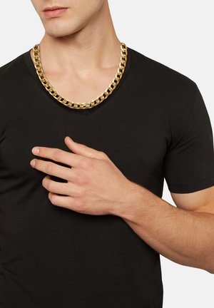 Collana in oro con maglie intrecciate, indossata sopra una t-shirt nera a scollo a V. La collana brilla, evidenziando il suo design audace e la sua texture.