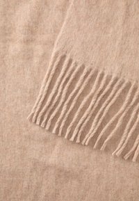 Lys beige uld sjal med tekstureret overflade og lange frynser på den ene kant, der har et blødt og varmt udseende.
