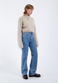 Beige fluffig tröja med långa ärmar, i kombination med högmidjade blå jeans och kraftiga svarta skor. Enkel design med minimala detaljer.