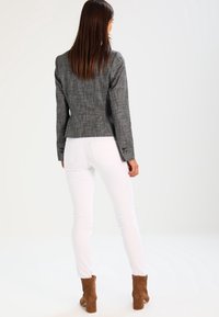 Blazer à carreaux gris avec un design ajusté, tissu texturé et poignets boutonnés, associé à un jean skinny blanc et des bottines à talons marron.