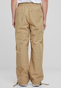 Beige casual fit broek van lichtgewicht materiaal met een elastische tailleband, voorzien van een achterzak en koordsluiting aan de onderkant.