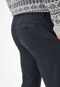 Donkerblauwe broek van een katoenmix, met een knoopzak aan de achterkant en een soepele textuur, met een gebreid trui zichtbaar erboven.
