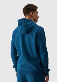 Sudadera azul hecha de una tela suave, con capucha ajustable, puños y dobladillo acanalados. Textura lisa con un ajuste relajado y sin logotipos visibles.