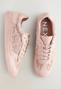 Rosa sneakers med texturerat blommigt tyg på sidorna, släta läderdetaljer, rund tå och platt gummisula. Har sex hål för snörning och snören.