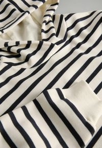 Nahaufnahme eines gestreiften Stoffes in Schwarz und Weiß, der die Kapuze und den gerippten Bund eines Langarmkleidungsstücks zeigt.