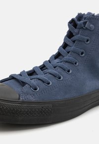 Høyhælte sneakers i marineblå semsket skinn med grå snørebånd, svart gummitåkappe og teksturert svart såledetalj.