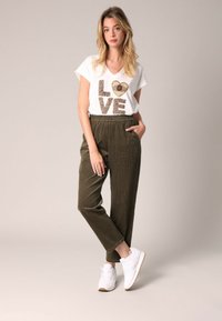 Witte v-hals t-shirt met "LOVE" in gouden en bruine glitter, gecombineerd met olijfgroene textuurbroek en witte sneakers.