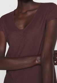 Bordöru V-hals T-paita lyhyillä hihoilla, valmistettu pehmeästä, tekstuuritetusta kankaasta. Kehonmyötäinen istuvuus tuo esiin kaulan ja käsien yksityiskohdat.