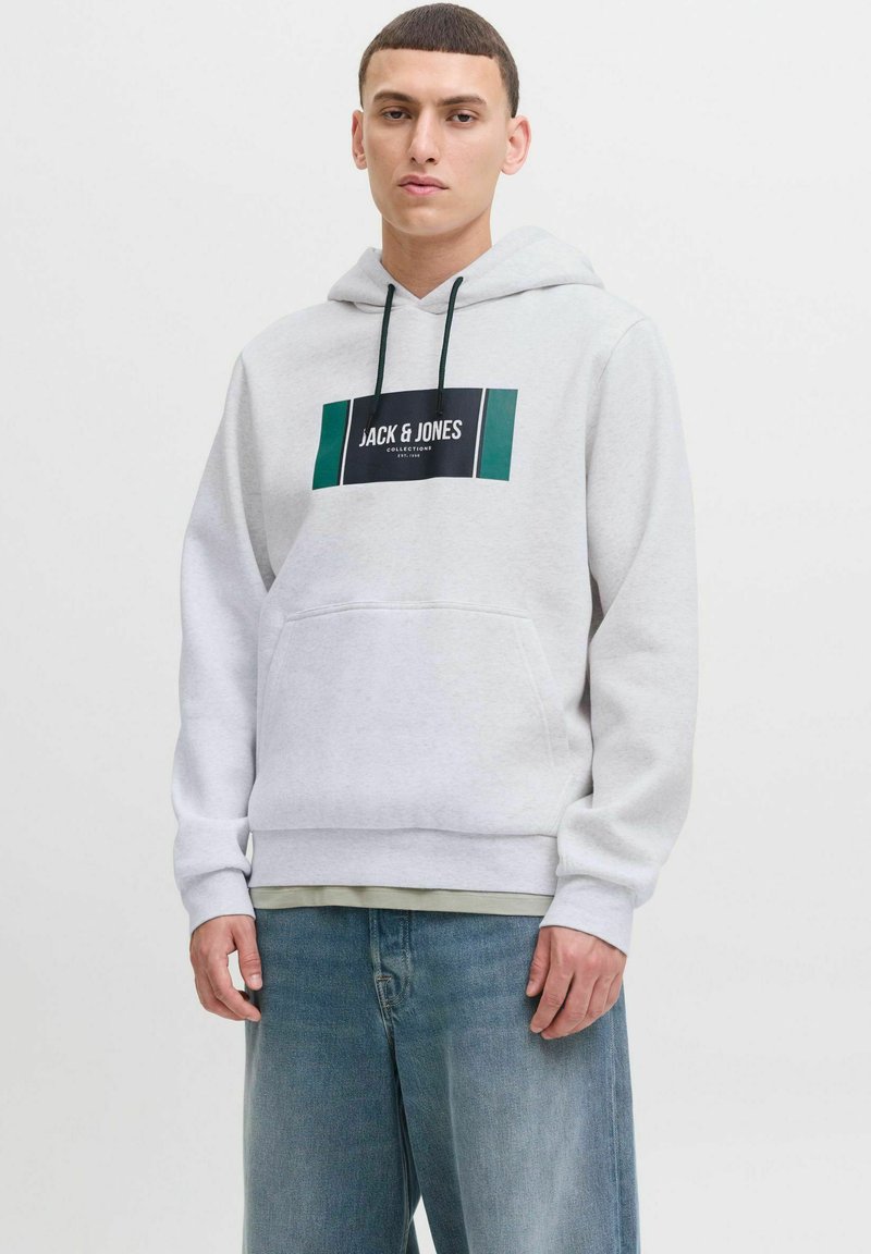 Grå hættebluse med en front kangaroo lomme, med sort og grøn logo tryk. Blødt stof, lange ærmer, ribbede mansjetter.