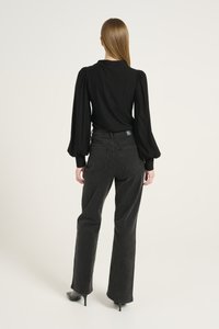 Black long-sleeve top with puffed shoulders paired with high-waisted black jeans. Model wears black heels, showcasing a smooth fabric texture.