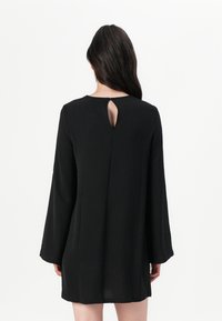 Vestido negro de manga larga con un corte relajado, que presenta un escote redondo y un detalle en forma de ojal en la parte posterior. Tejido suave y texturizado.