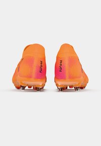 Jasnopomarańczowe korki piłkarskie z teksturowanym wykończeniem, z różowym gradientem, lekką konstrukcją i przezroczystymi, przejrzystymi korkami.