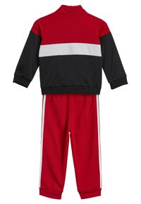 Chándal rojo y negro con cuello alto, franja horizontal blanca en el pecho y franjas blancas a los lados de los pantalones.