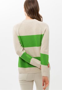 Pull beige avec de larges rayures vertes, texture tricotée et manches à côtes. Le design comprend des manches raglan et un col rond classique.