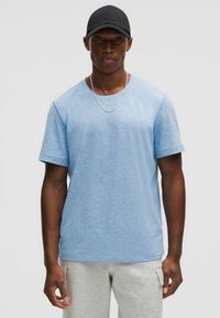 Light blue short-sleeve t-shirt with a round neckline, made of a soft fabric, paired with gray sweatpants. Two silver chains are visible.