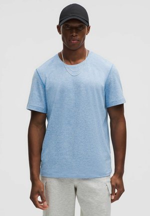 Light blue short-sleeve t-shirt with a round neckline, made of a soft fabric, paired with gray sweatpants. Two silver chains are visible.