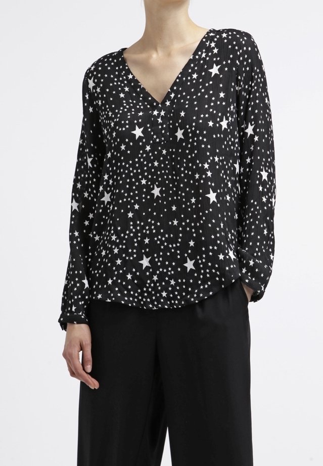 Blouse noire à manches longues et col en V, avec un motif d'étoiles blanches. Tissu léger et texturé avec une coupe décontractée.
