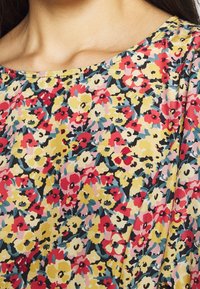 Bluse mit Blumenmuster, die ein mehrfarbiges Design auf einem hellen Hintergrund zeigt. Rundhalskragen mit lockerem, atmungsaktivem Stoff und kurzen Ärmeln.