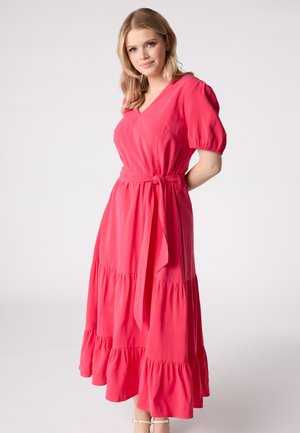 Robe maxi rose à volants avec un décolleté en V, des manches bouffantes et une ceinture nouée. Tissu doux avec un ourlet à volants qui tombe fluidement.