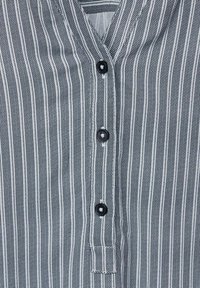 Gestreepte shirt met zwart-witte verticale lijnen, met een V-hals en drie zwarte knopen aan de voorkant, van gestructureerde stof.