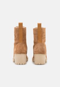 Bottines en daim tan avec un dos renforcé, semelles en caoutchouc beige et détails de couture. Le design comprend une languette pour un enfilage facile.