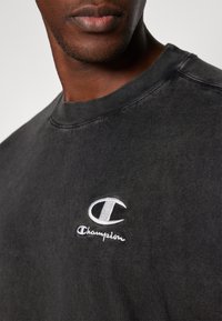 Schwarzes Sweatshirt aus Baumwolle, mit Rundhalsausschnitt, strukturiertem Finish und einem weißen gestickten Champion-Logo auf der linken Brust.