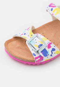 Valkoinen sandaali, jossa on värikäs abstrakti kuvio, hopeinen solki, korkkipohja ja vaaleanpunainen kumipohja.