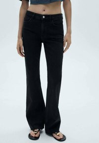 Mustat leveälahkeiset farkut, joissa on viisi taskua, keski-korkea vyötärö ja hienovarainen tekstuuri. Yhdistetty mustiin sandaaleihin.