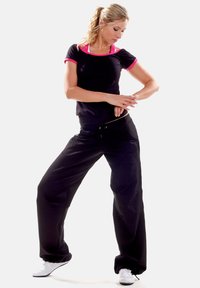 Black athletic outfit with pink accents; fitted short-sleeve top and loose, tapered pants; textured fabric; white sneakers.