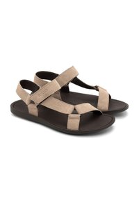 Beige suede sandaalid kahe laia rihmaga, reguleeritava pahkluu rihmaga ja tumeda pruuniga lame tallaga. Suvine ja mugav disain, sobib sooja ilma jaoks.