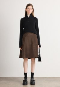 Pullover nero in maglia con mezza zip, gonna in velluto a coste marrone, scarpe platform nere e calze frills fino al ginocchio. Borsa semplice tra le mani.