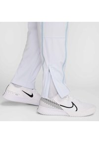 HVITE treningsbukser med lyseblå sidesømmer og glidelås ved anklene, kombinert med hvite og svarte Nike-sko med stripete design.