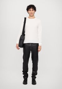 Hvid langærmet striktop, sorte læderbukser med lynlås foran, og sorte læderstøvler. Sort crossbody taske med justerbar strop.