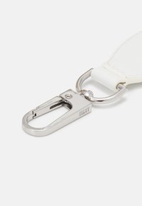 Clip de mousqueton en métal avec finition argentée brillante, attaché à une sangle en faux cuir blanc avec des détails de couture, affichant la marque DKNY.