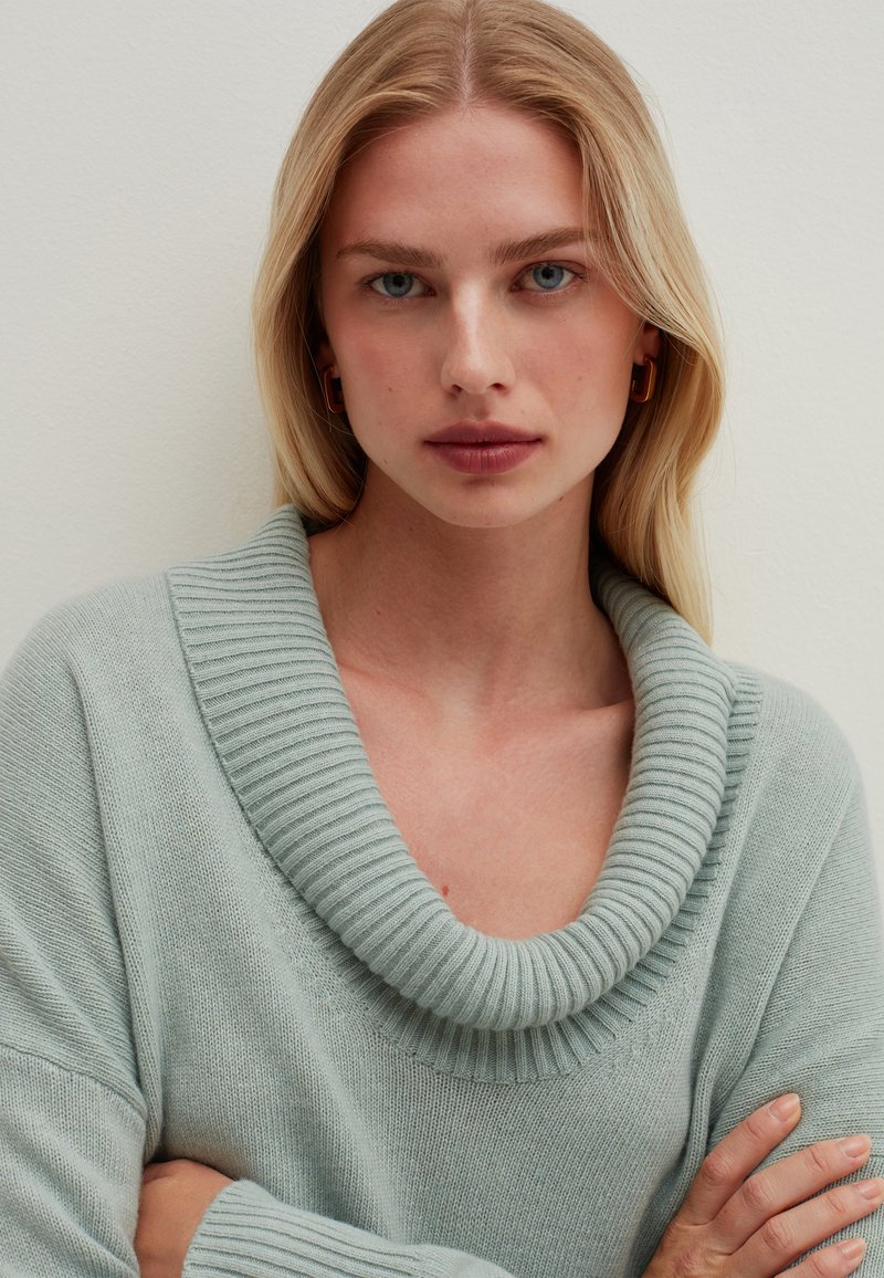 Hellblaues Oversize-Pullover mit einem gerippten Kragen und weiten Ärmeln. Die Textur wirkt weich und gestrickt.