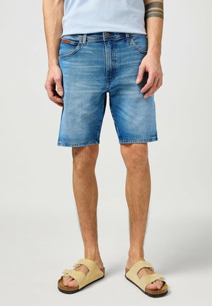 Denim shorts in light blue with a classic five-pocket design, straight cut, and frayed hem. Paired with beige sandals.