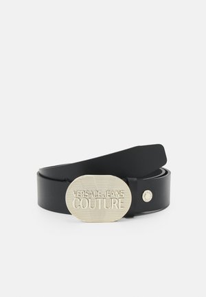 Cinturón de cuero negro con hebilla ovalada grande de plata grabada con el texto "Versace Jeans Couture" en un patrón de rayas.