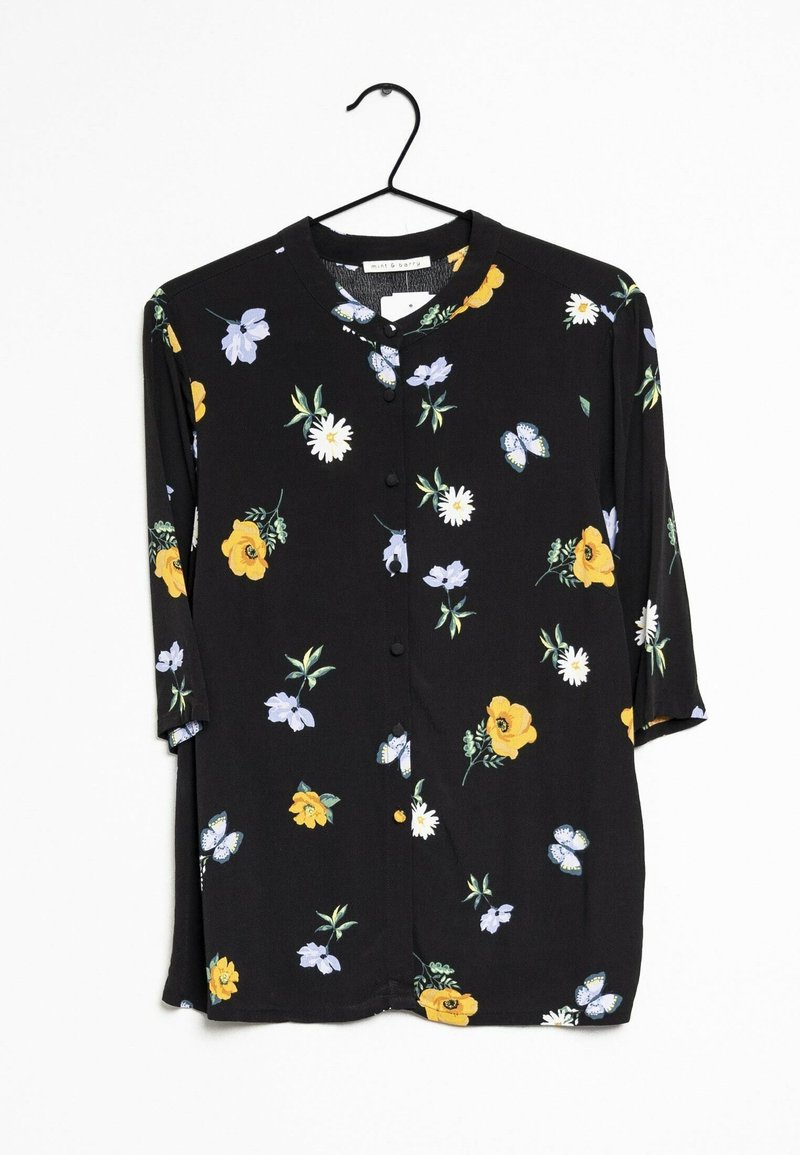 Chemise noire à manches longues boutonnée avec un imprimé floral et papillons jaune, blanc et violet clair, accrochée à un cintre noir.